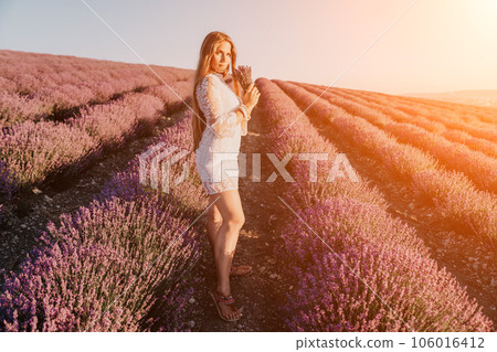Woman lavender field. Happy carefree woman in a white dress walking in a lavender field and smelling a lavender bouquet on sunset. Ideal for warm and inspirational concepts in wanderlust and travel. 106016412