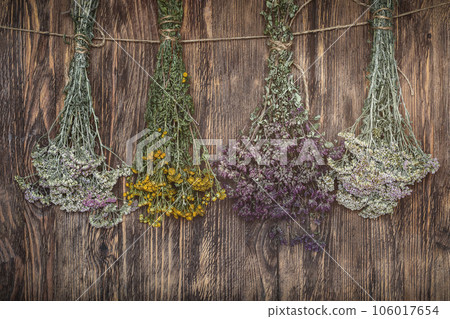 Bundles of dried herbs hang on a string on wooden background, oregano, tansy, yarrow. 106017654