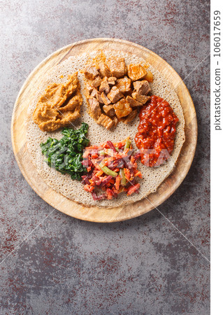 Meal consisting of injera and several kinds of wat or tsebhi stew is typical of Ethiopian cuisine closeup. Vertical top view Meal consisting of injera and several kinds of wat or tsebhi stew is typical of Ethiopian cuisine closeup. Vertical top view 106017659