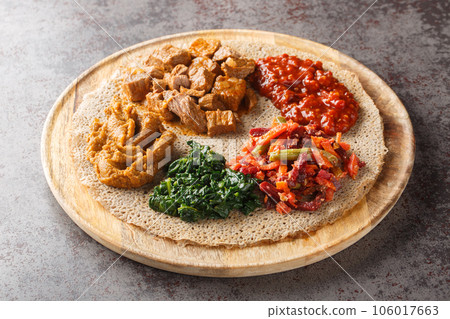 Injera is a sourdough flatbread made from teff flour served with filling close up on the wooden board. Horizontal Injera is a sourdough flatbread made from teff flour served with filling close up on the wooden board. Horizontal 106017663