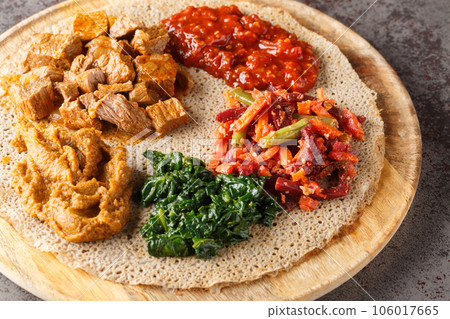 Ethiopian Injera topped with meat, vegetables, greens close up on the wooden board. Horizontal 106017665