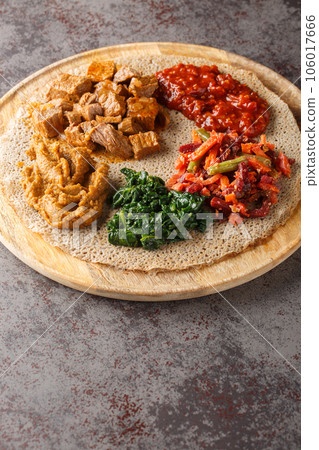 Meal consisting of injera and several kinds of wat or tsebhi stew is typical of Ethiopian cuisine closeup. Vertical Meal consisting of injera and several kinds of wat or tsebhi stew is typical of Ethiopian cuisine closeup. Vertical 106017666