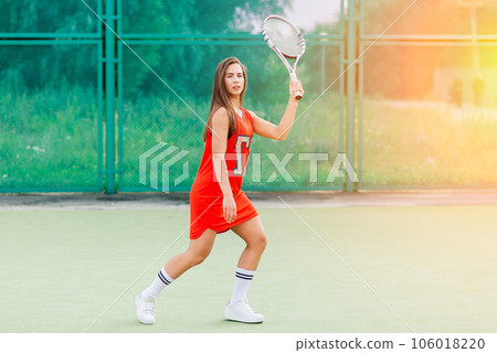 Beautiful female tennis player on tennis court. Red dress. 106018220