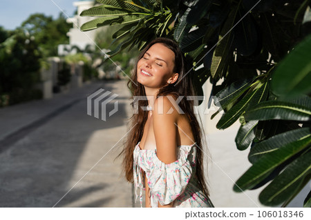 Young beautiful woman in a romantic dress with a floral print, and a pearl necklace bracelet, against the backdrop of tropical leaves Young beautiful woman in a romantic dress with a floral print, and a pearl necklace bracelet, against the backdrop of tropical leaves 106018346