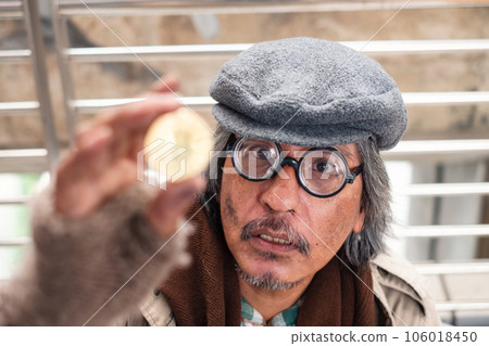 Aged homeless beggar staring at gold coin with excitement 106018450