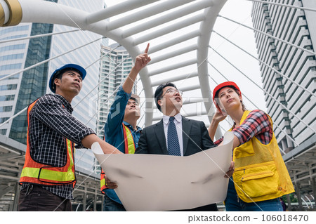 Team of engineer with businessman holding blueprint meeting and discussing for a new project in construction site 106018470