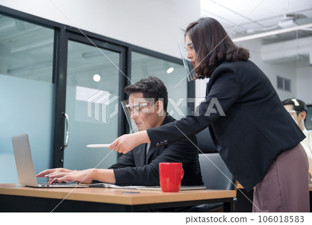 Bossy manager female ordering and pointing at laptop of office male worker wearing face shield at the office Bossy manager female ordering and pointing at laptop of office male worker wearing face shield at the office 106018583