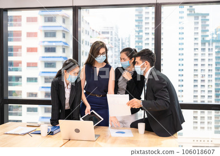 Multiethnic business team wearing face mask during business meeting in new normal office. Diverse corporate colleagues brainstorming with technology device Multiethnic business team wearing face mask during business meeting in new normal office. Diverse corporate colleagues brainstorming with technology device 106018607