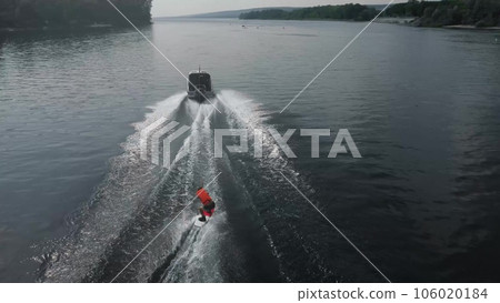A young man rides a wakeboard. A sports guy rides on the water on a board behind a boat. Top view from a drone. 106020184
