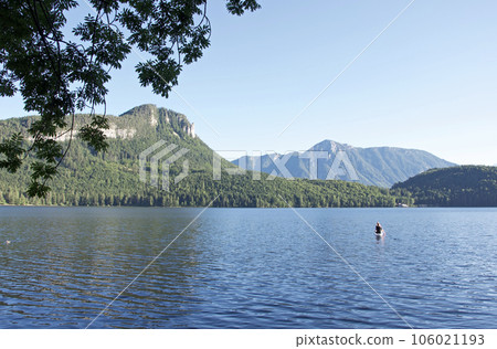 Landscape of Lake Altaussee in Austria and a person sitting and rowing on a SUP paddle (person is back view) 106021193