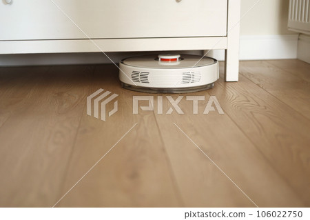 Wireless autonomous robotic vacuum cleaner vacuums with brushes under commode at living room. Self-propelled cleaning robot. Household remote control appliances. Smart cleaning technology. 106022750