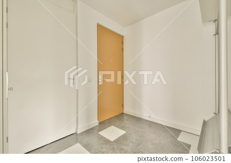 an empty room with white walls and grey flooring, there is a bright orange door in the center of the room 106023501