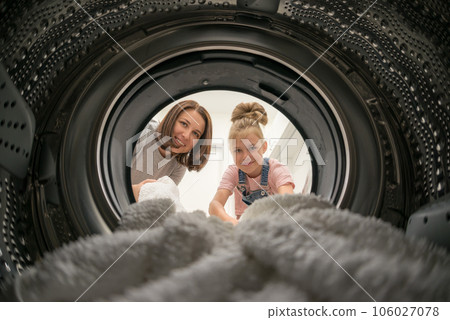 Woman Doing Laundry with her daughter Reaching towel Inside Washing Machine, view from inside Woman Doing Laundry with her daughter Reaching towel Inside Washing Machine, view from inside 106027078