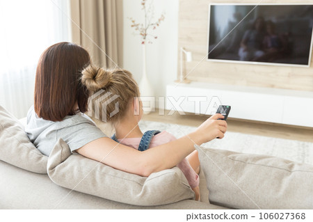 Mother and daughter sitting on sofa watching tv Mother and daughter sitting on sofa watching tv 106027368