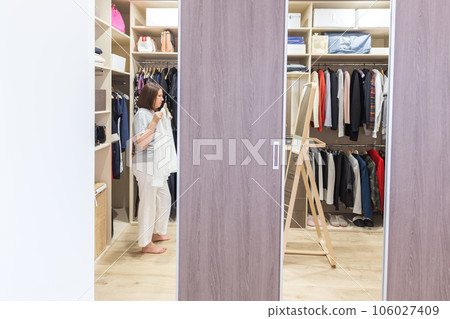 Woman in big walkin closet choosing clothes. modern wardrobe and dressing room with copy space Woman in big walkin closet choosing clothes. modern wardrobe and dressing room with copy space 106027409