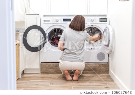 Woman Loading Dirty Clothes In Washing Machine For Washing In modern Utility Room Woman Loading Dirty Clothes In Washing Machine For Washing In modern Utility Room 106027648