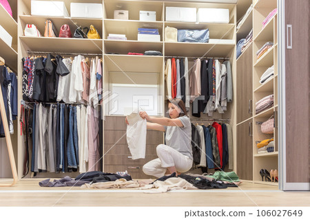 Young woman throwing clothes in walk in closet. Mess in wardrobe and dressing room Young woman throwing clothes in walk in closet. Mess in wardrobe and dressing room 106027649