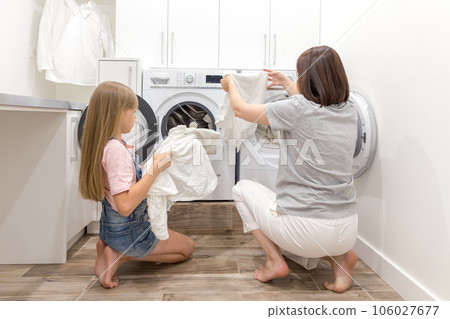 Girl helping her mother in laundry room Girl helping her mother in laundry room 106027677