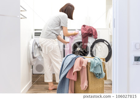 Woman Loading Dirty Clothes In Washing Machine For Washing In modern Utility Room Woman Loading Dirty Clothes In Washing Machine For Washing In modern Utility Room 106027815