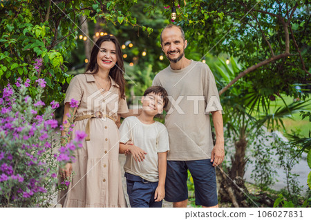 A loving family enjoying a leisurely walk in the park - a radiant pregnant woman after 40, embraced by her husband, and accompanied by their adult teenage son, savoring precious moments together 106027831