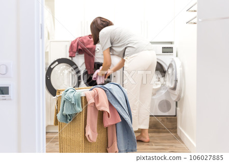Young Woman loading washing machine and a Basket Full Of Dirty Clothes In Laundry Room Young Woman loading washing machine and a Basket Full Of Dirty Clothes In Laundry Room 106027885