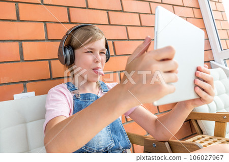 A young girl showing tongue enjoying listening to music on her headphone with tablet 106027967