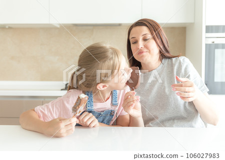 Mother with daughter in kitchen eating ice cream. Good relations of parent and child. Happy family concept 106027983