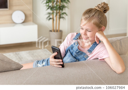 Little girl playing with a cell phone at home on a couch 106027984