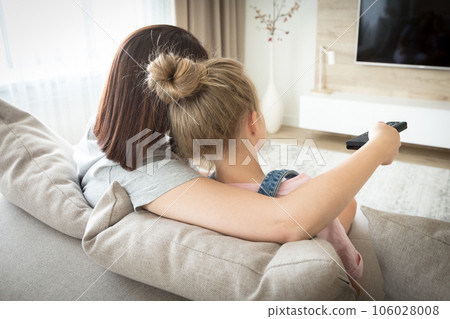 Mother and daughter sitting on sofa watching tv 106028008