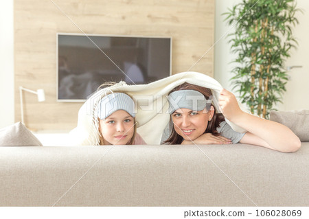 Mother and daughter wearing sleeping mask having fun on couch with copy space Mother and daughter wearing sleeping mask having fun on couch with copy space 106028069