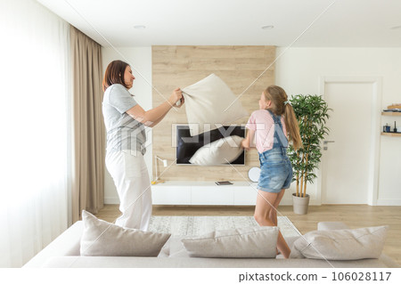 Happy family games. Single mother and her child girl are fighting pillows and jumping on couch 106028117