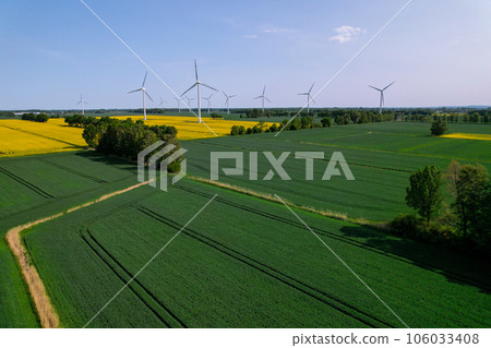 Aerial view Wind turbine on grassy yellow farm canola field against cloudy blue sky in rural area. Offshore windmill park with clouds in farmland Poland Europe. Wind power plant generating electricity 106033408