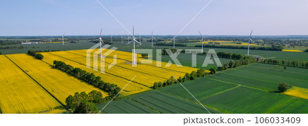 Aerial view Wind turbine on grassy yellow farm canola field against cloudy blue sky in rural area. Offshore windmill park with clouds in farmland Poland Europe. Wind power plant generating electricity 106033409