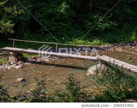 Wooden bridge over river with turquoise waters and rocky riverbed in the forest 106033492
