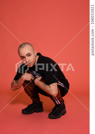 Studio shot of a young tattoed bald man posing against a pink background. 90s style. Studio shot of a young tattoed bald man posing against a pink background. 90s style. 106033921
