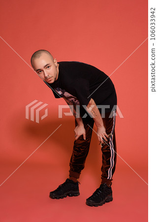 Studio shot of a young tattoed bald man posing against a pink background. 90s style. Studio shot of a young tattoed bald man posing against a pink background. 90s style. 106033942