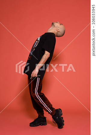 Studio shot of a young tattoed bald man posing against a pink background. 90s style. 106033945