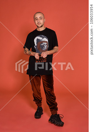 Studio shot of a young tattoed bald man posing against a pink background. 90s style. 106033954