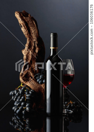 Bottle and glass of red wine with an old snag and blue grapes. 106036176