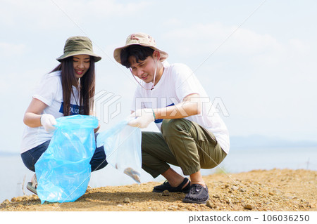 Group of Asian young people volunteer helping to collecting or picking up a plastic bottle garbage on the ground in park. Sustainability and environment conservation concept. 106036250