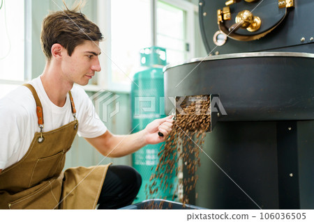 Professional male and female coffee roasters working with modern automated roasting machine in the coffee roasting factory. Coffee roasters checking or inspecting the roasting quality of coffee bean. 106036505