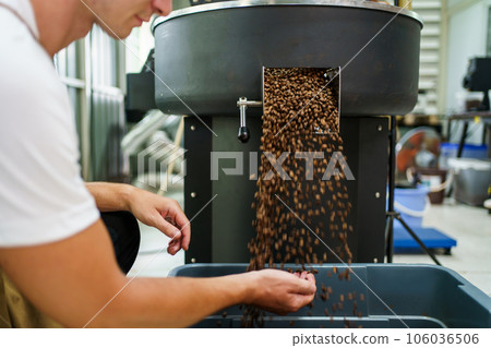 Professional male and female coffee roasters working with modern automated roasting machine in the coffee roasting factory. Coffee roasters checking or inspecting the roasting quality of coffee bean. 106036506