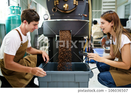 Professional male and female coffee roasters working with modern automated roasting machine in the coffee roasting factory. Coffee roasters checking or inspecting the roasting quality of coffee bean. Professional male and female coffee roasters working with modern automated roasting machine in the coffee roasting factory. Coffee roasters checking or inspecting the roasting quality of coffee bean. 106036507