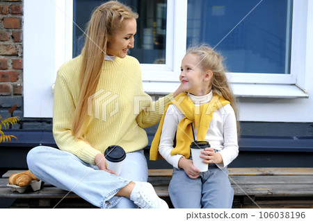 Mom and daughter are sitting on a bench with glasses of hot chocolate and croissants. The family spends the weekend together. Mom and daughter are sitting on a bench with glasses of hot chocolate and croissants. The family spends the weekend together. 106038196