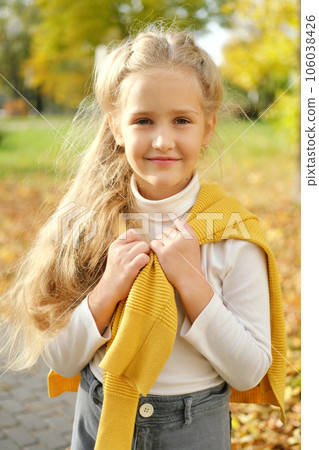 Little blonde preschool girl in jeans, turtleneck and sweater posing for the camera in the autumn park 106038426