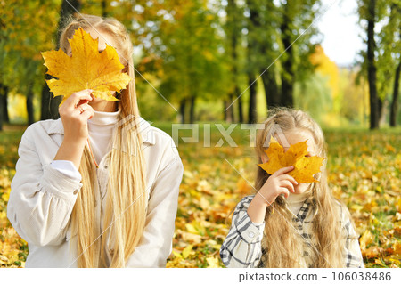 The family spends time together in the park. Girl and mother sit on a blanket and cover their faces with autumn leaves The family spends time together in the park. Girl and mother sit on a blanket and cover their faces with autumn leaves 106038486