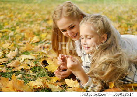 The Caucasian family has fun in the park. Girl and mother lie on a blanket and look at autumn leaves The Caucasian family has fun in the park. Girl and mother lie on a blanket and look at autumn leaves 106038514