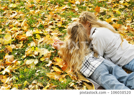 The family has fun in the park. The girl and mother lie on a blanket with their backs to the camera and look at the autumn leaves. 106038520