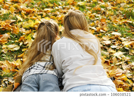 The family has fun in the park. The girl and mother lie on a blanket with their backs to the camera and look at the autumn leaves. 106038521