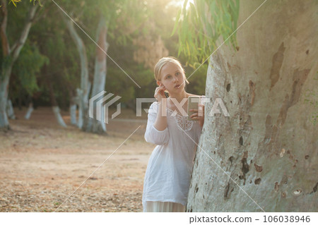 Teenage girl in white shirt lisening to music in headphones on the background of forest Teenage girl in white shirt lisening to music in headphones on the background of forest 106038946